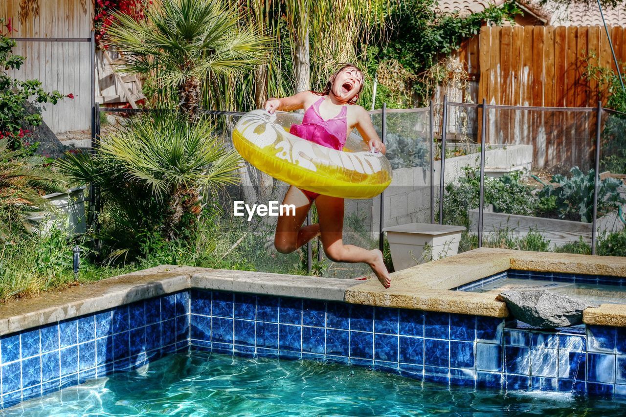 Full length of happy girl with inflatable ring jumping into swimming pool