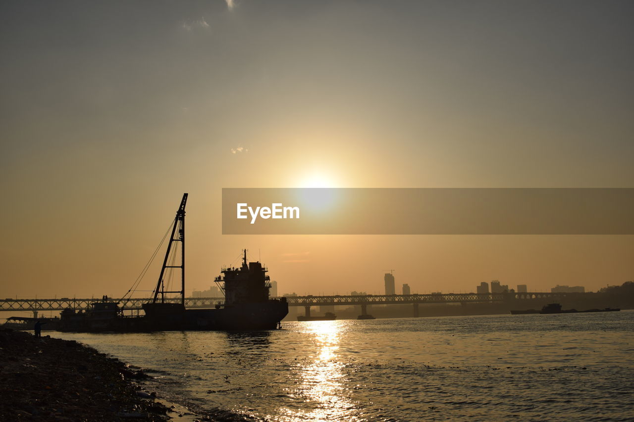 Scenic view of river against bright sun in sky during sunset