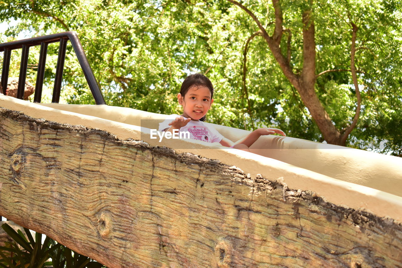 Low angle view of girl on slide against trees at amusement park