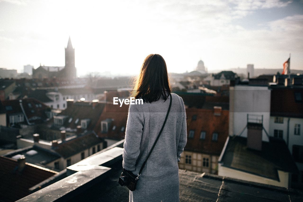 Rear view of mid adult woman standing by cityscape against sky