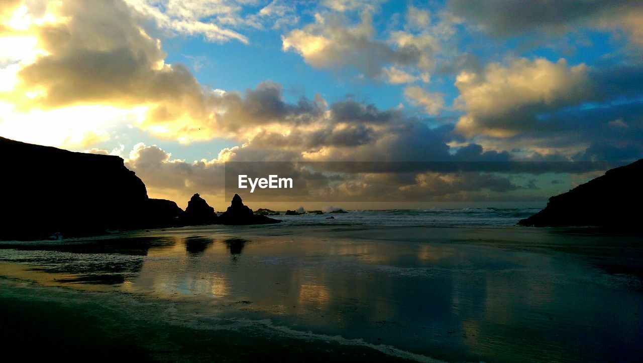 Silhouette rocks on beach against cloudy sky during sunset