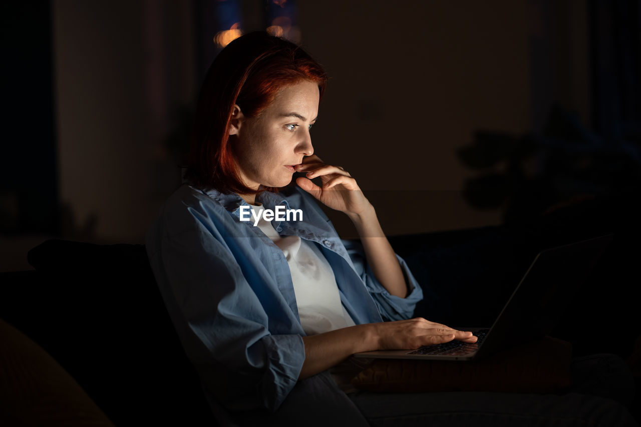 Focused freelancer woman looking laptop screen at night working from home.
