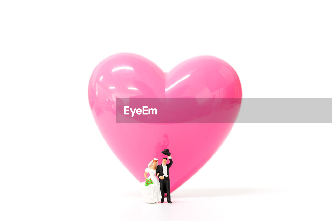 Close-up of figurine and heart shaped balloon against white background