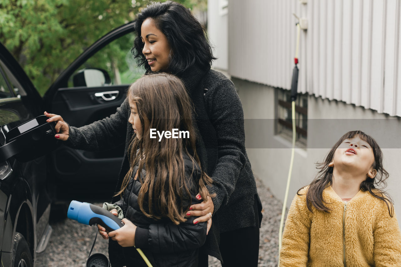 Woman teaching daughter to charge electric car at charging station