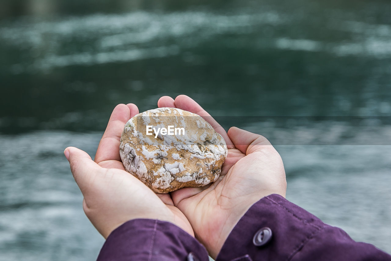 Close-up of hand holding stone over water