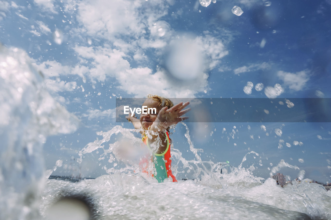 Girl playing in sea against cloudy sky