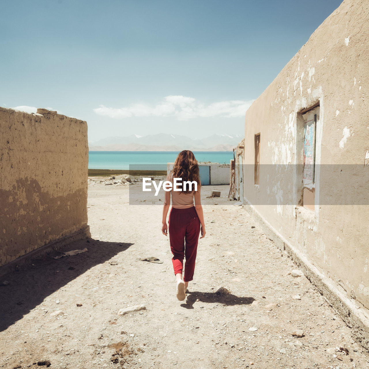 FULL LENGTH REAR VIEW OF WOMAN WALKING ON SEA AGAINST BUILDINGS