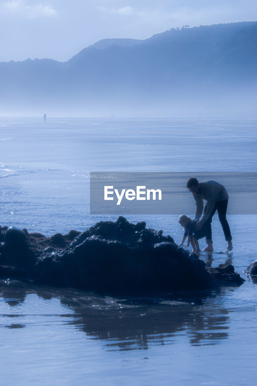 water, ocean, wave, sea, nature, coast, one person, sky, silhouette, beauty in nature, surfing, mountain, wind wave, men, scenics - nature, adult, land, full length, leisure activity, environment, sports, beach, shore, horizon, blue, lifestyles, outdoors, person, adventure, motion, day, tranquility, holiday, activity, vacation, landscape, reflection, side view, trip, travel, tranquil scene, non-urban scene, standing, cold temperature, travel destinations