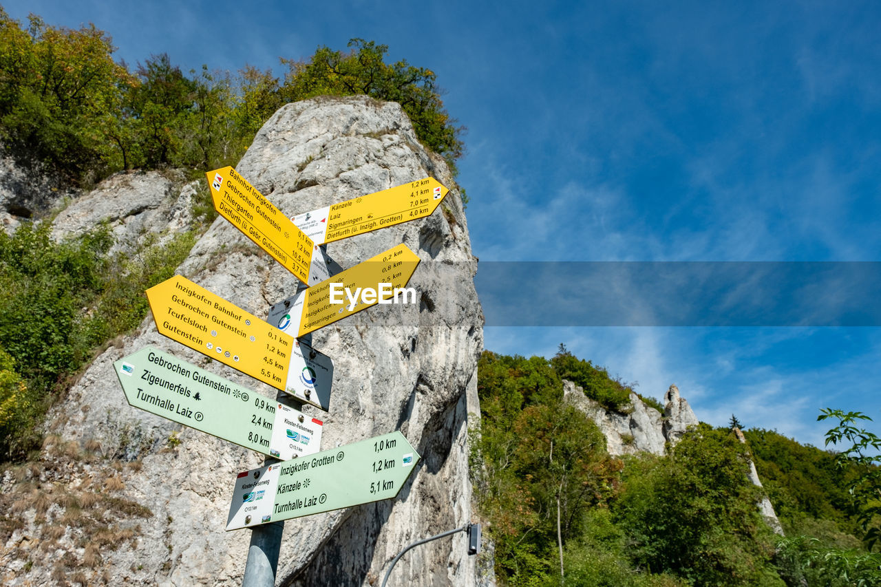 Low angle view of sign on rock against sky