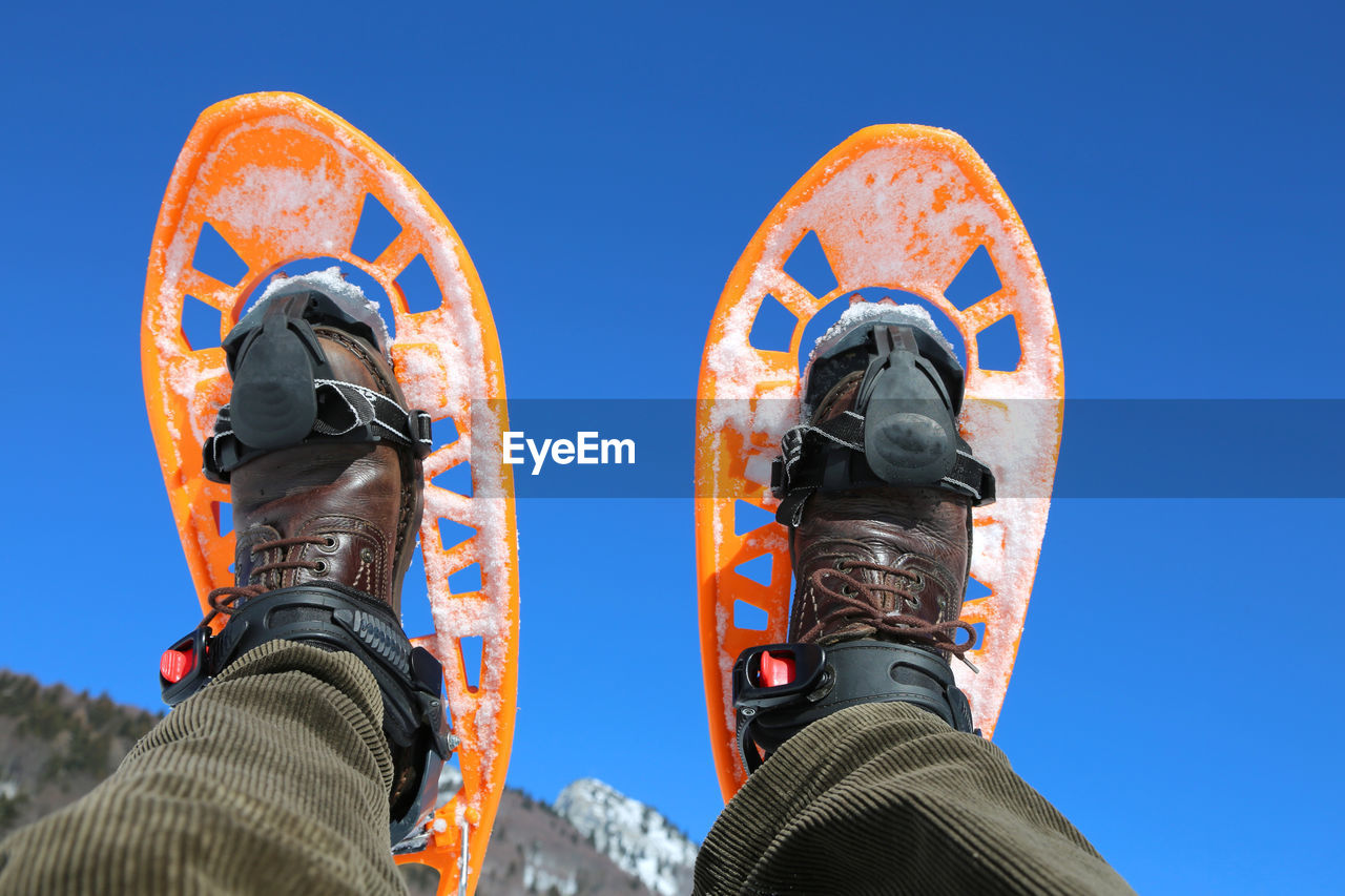 Low section of person wearing snowshoe against clear blue sky