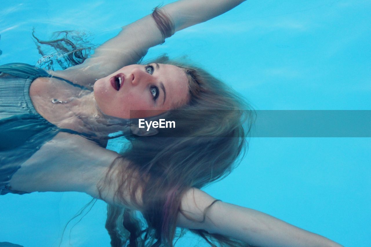 High angle view of young woman with mouth open swimming in pool
