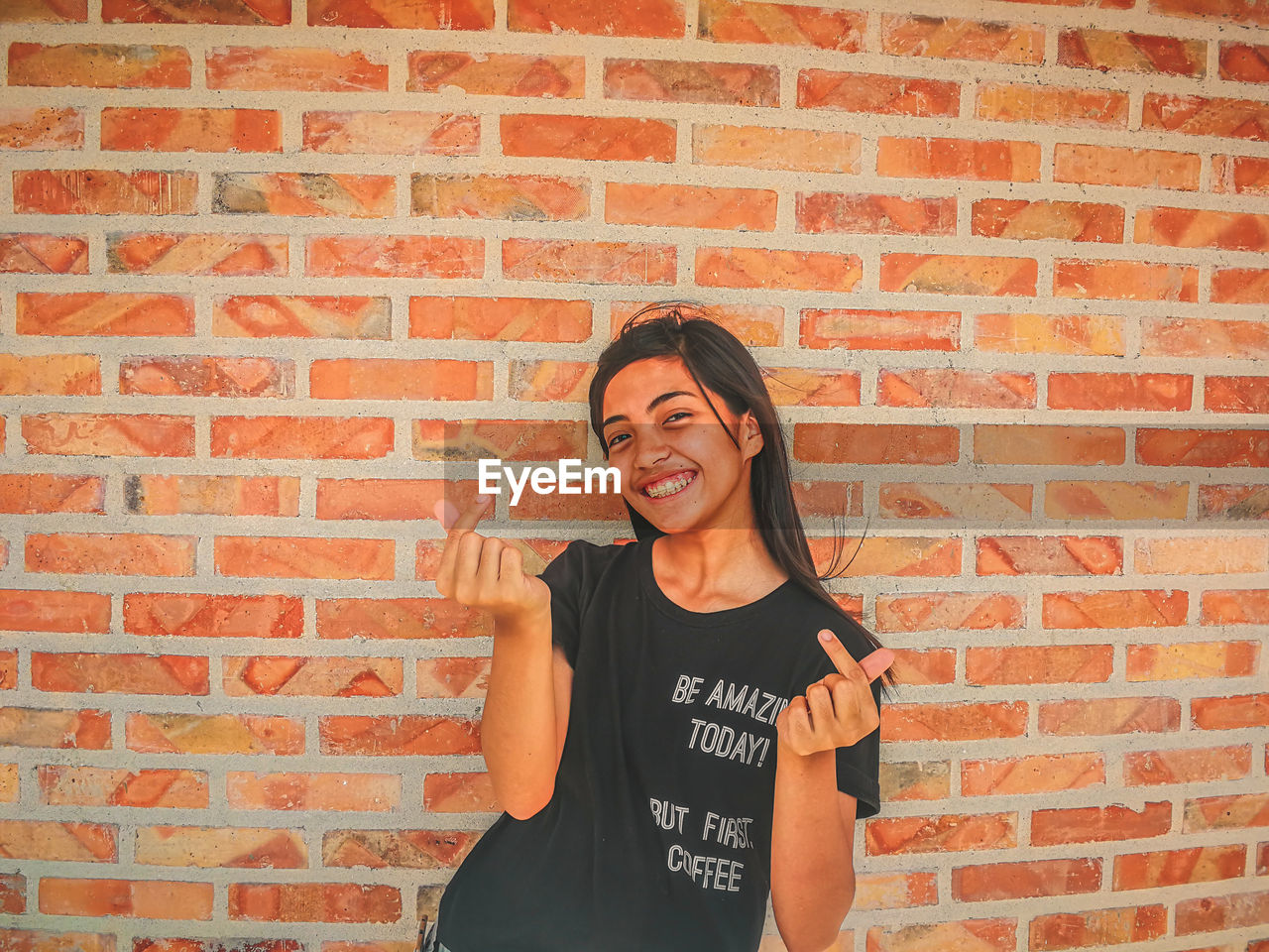 Portrait of smiling teenage girl gesturing against brick wall