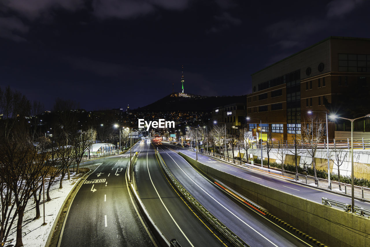 LIGHT TRAILS ON ROAD AMIDST ILLUMINATED BUILDINGS IN CITY