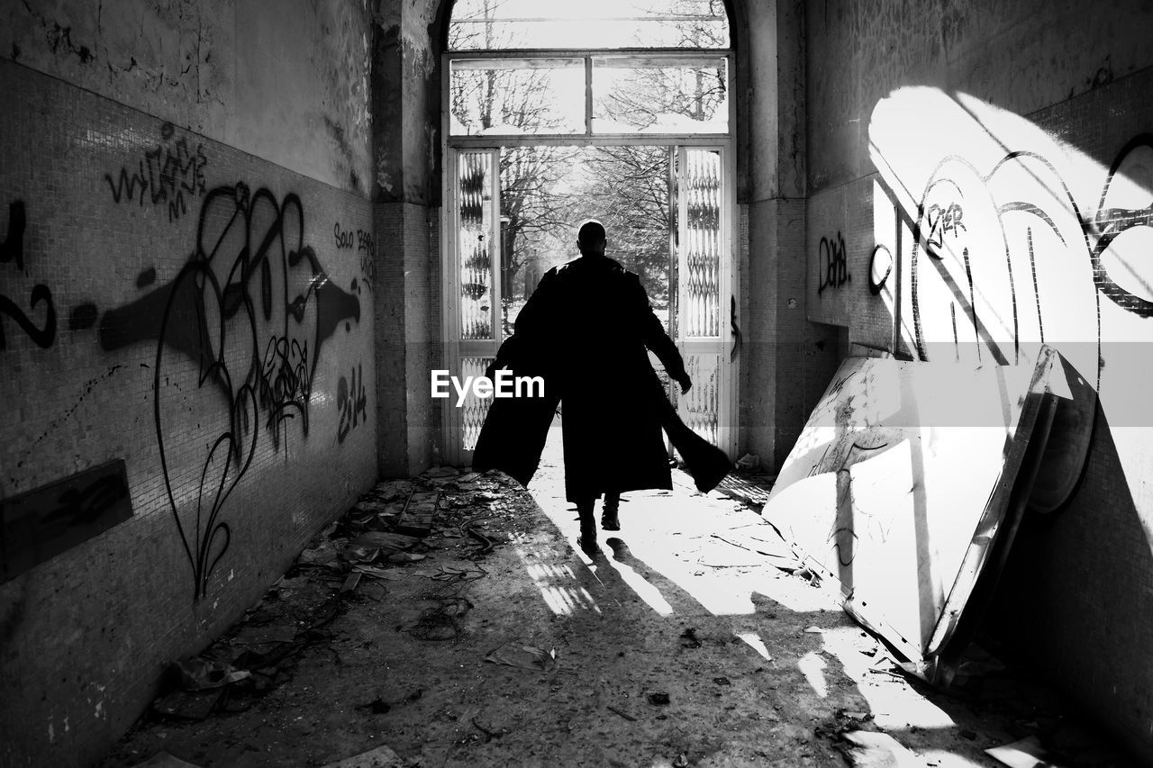 REAR VIEW OF MAN WALKING ON ABANDONED BUILDING