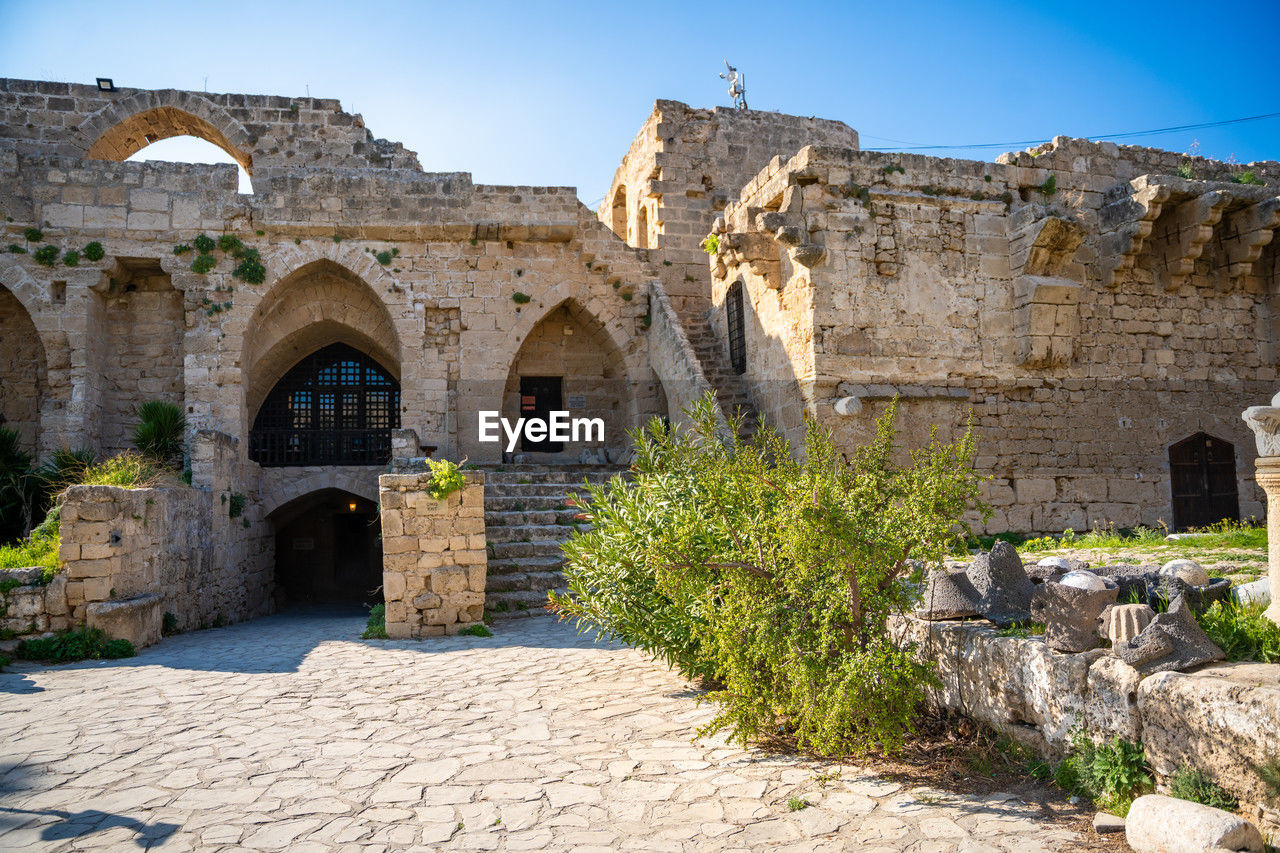 architecture, history, the past, ruins, ancient history, built structure, fortification, ancient, arch, travel destinations, nature, building, building exterior, travel, old, historic site, clear sky, wall, tourism, old ruin, stone material, blue, vacation, sky, no people, sunny, estate, plant, village, outdoors, rock, medieval, religion, stone wall, city, sunlight, day