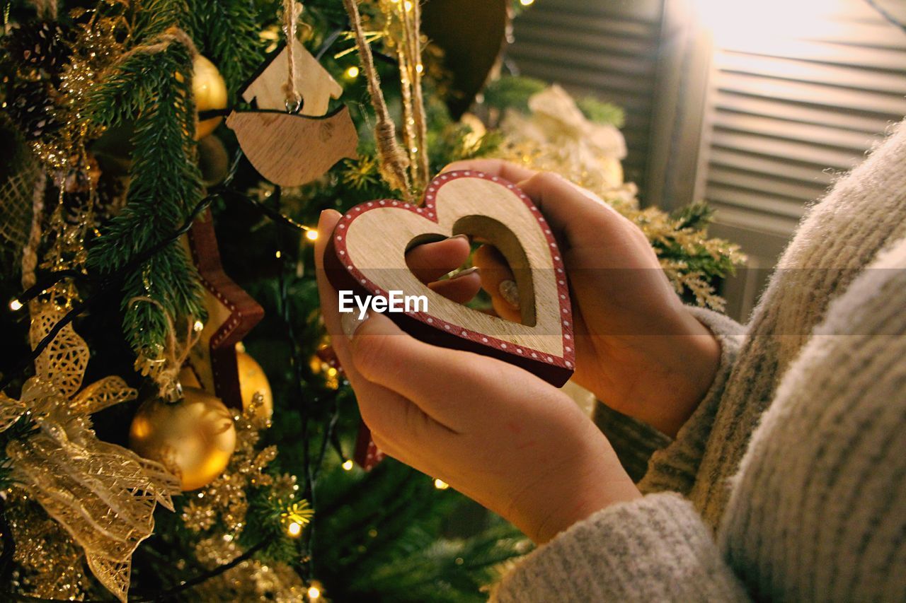 Midsection of woman holding heart shaped ornament on christmas tree