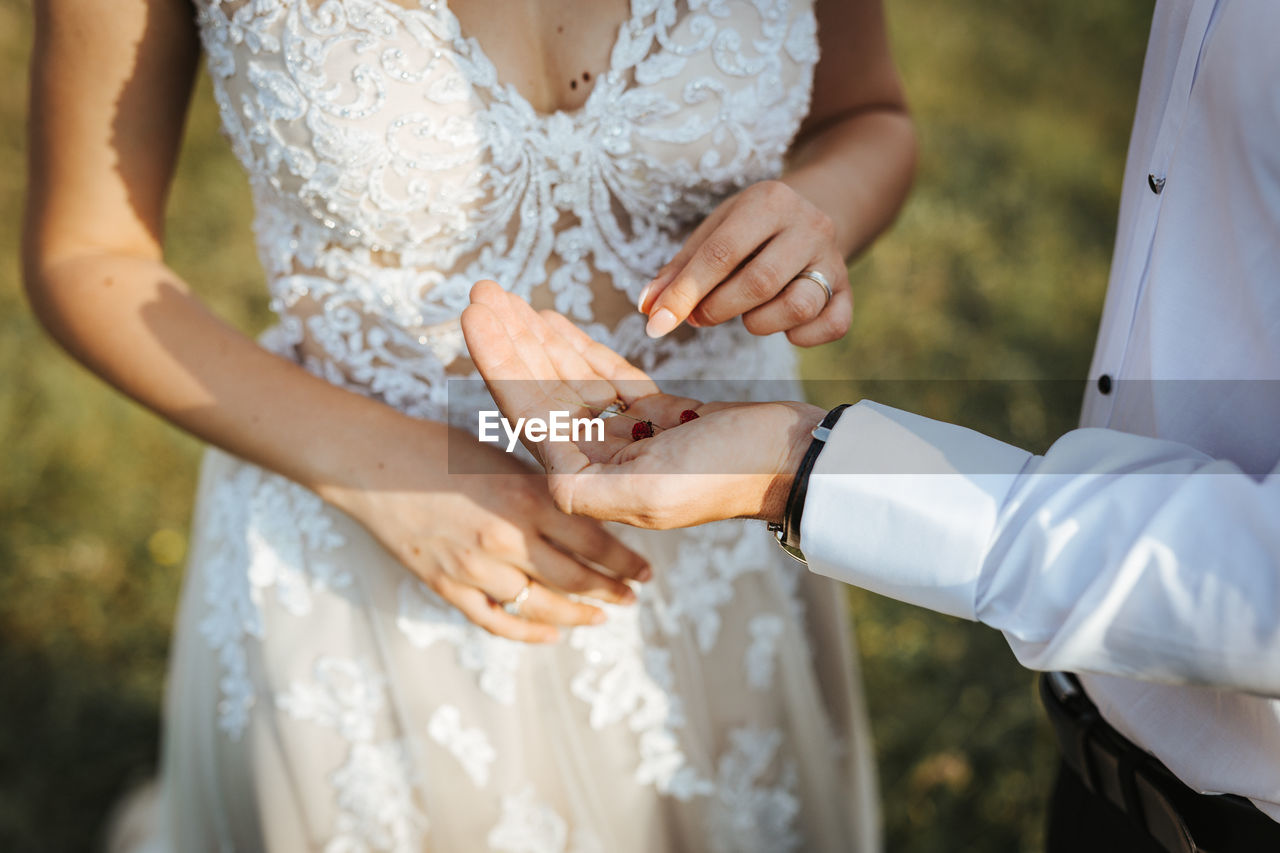 Midsection of bride giving berries on grooms hand