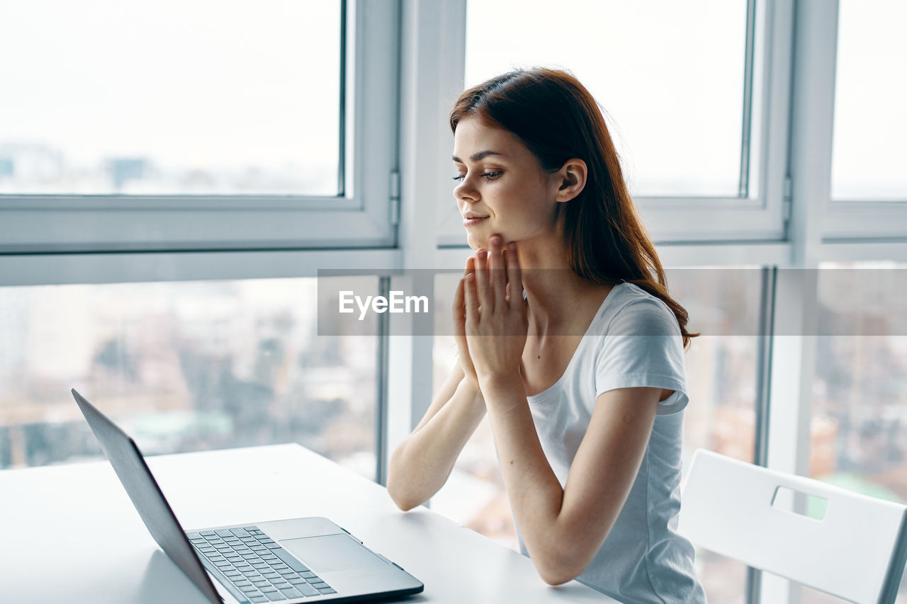 YOUNG WOMAN USING LAPTOP ON TABLE