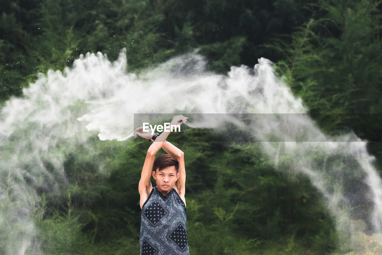 Portrait of man throwing sand mid-air against plants