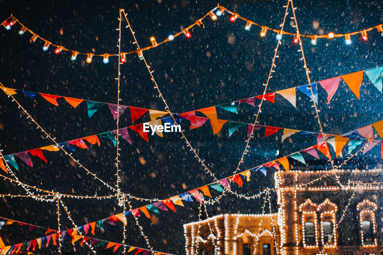 Flying snow in the evening light in festive magic new year atmosphere with garlands and flags