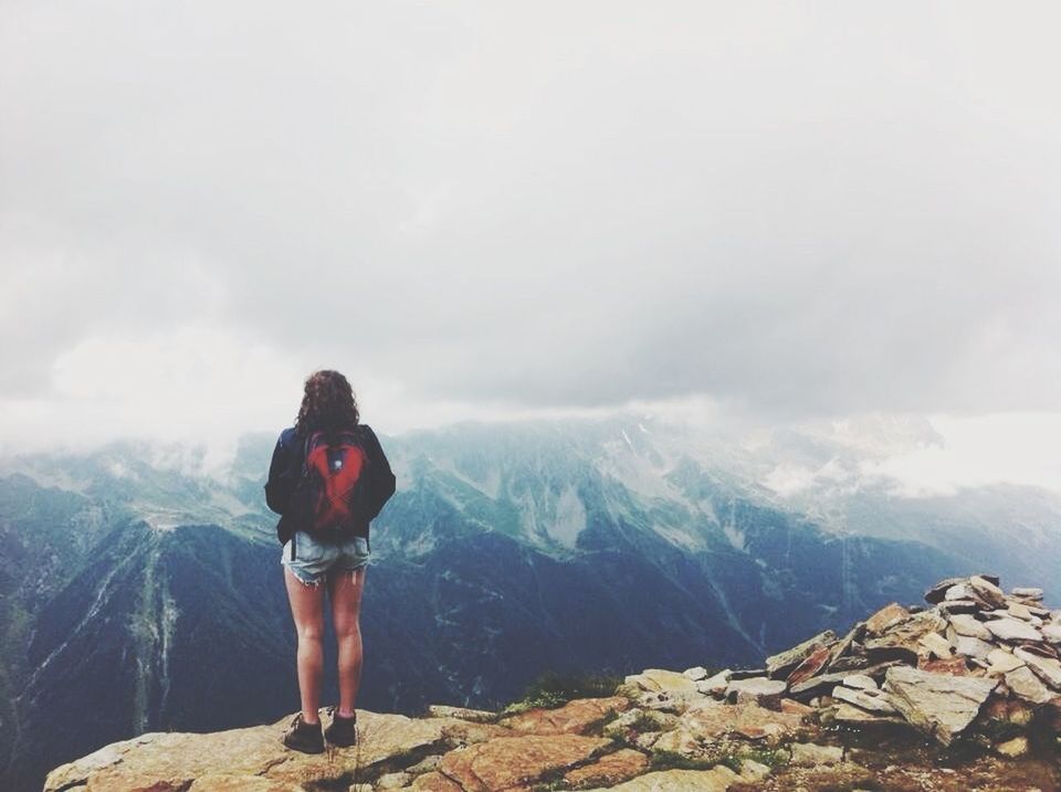 Full length rear view of woman standing on rock against mountains