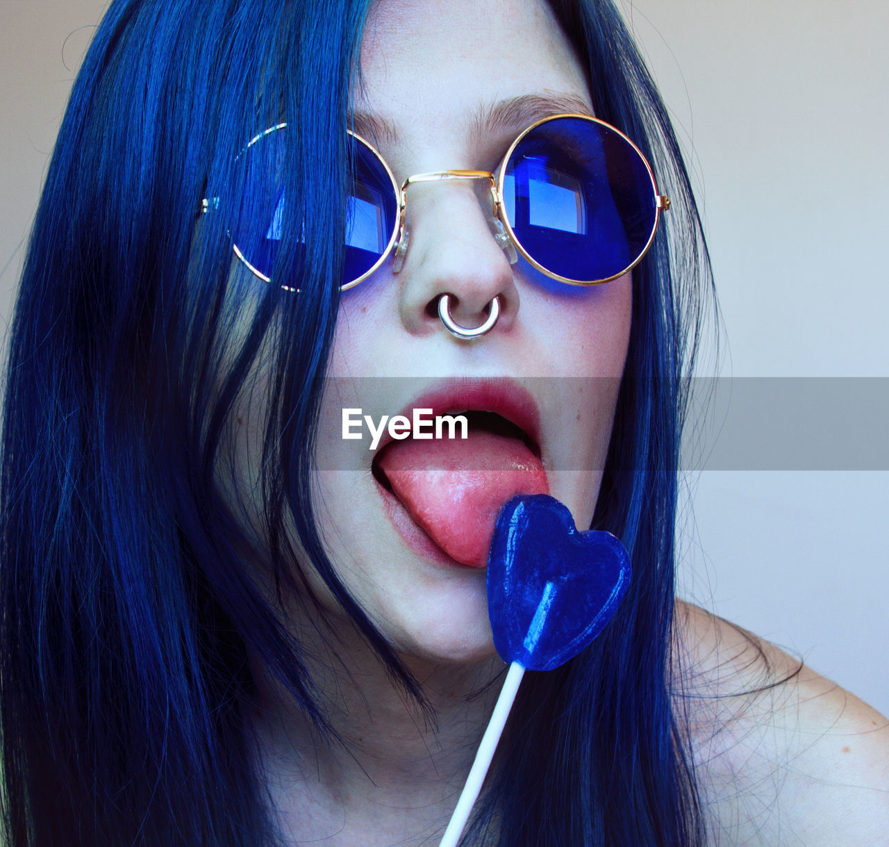 Young woman wearing blue sunglasses licking heart shape candy