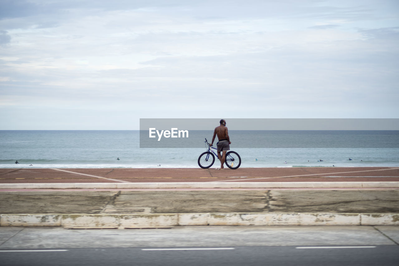 MAN RIDING BICYCLE IN SEA AGAINST SKY