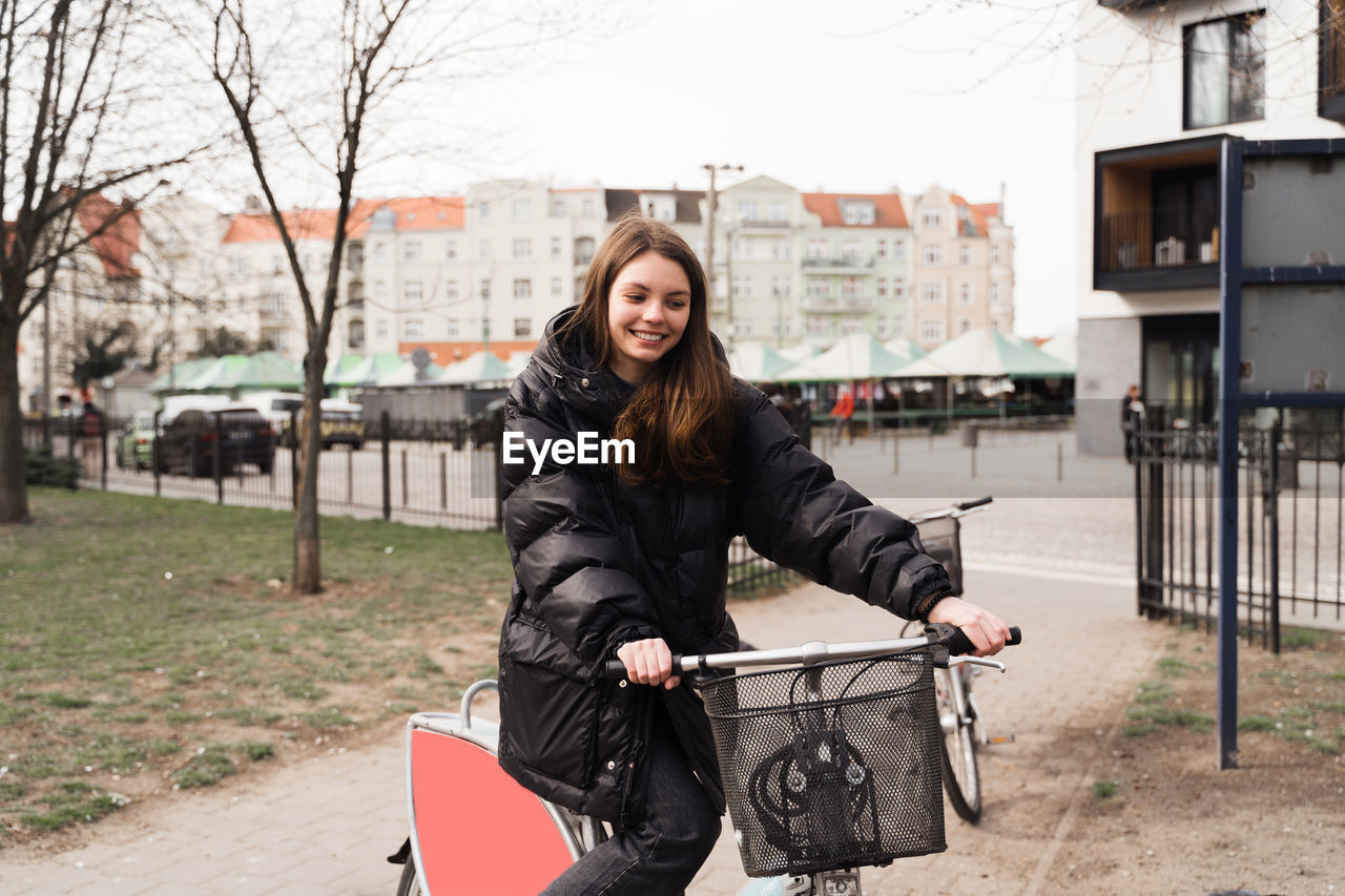 Happy young woman with bicycle standing on footpath