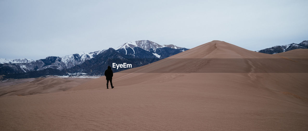 Full length of man walking on arid landscape against mountains and sky
