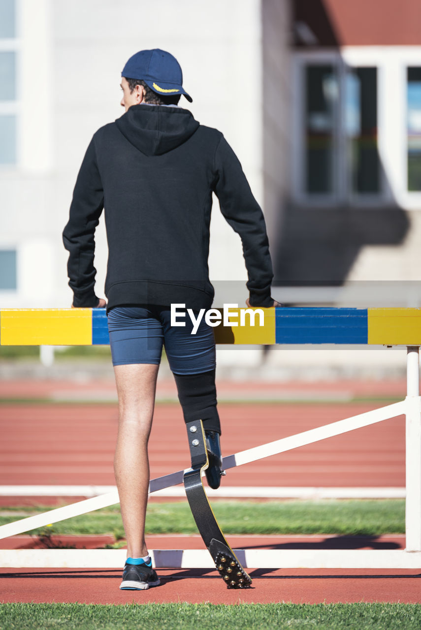Rear view of athlete with prosthetic leg while standing by railing
