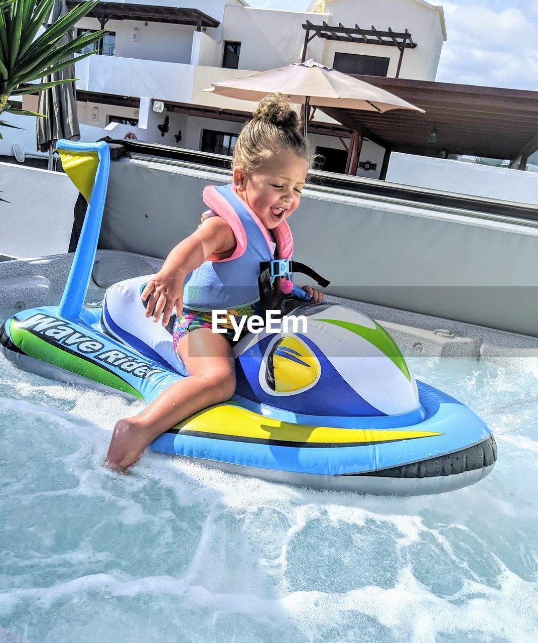 Toddler in jacuzzi on inflatable jet ski. 