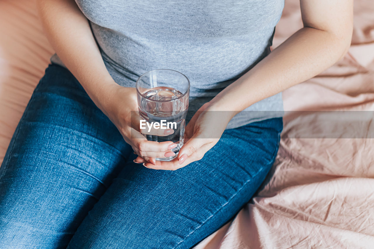 Woman sits in bed and holds glass of clean water in her hands. world water day. health care concept.