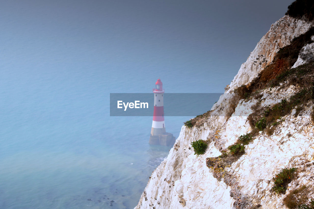 Lighthouse by sea against clear sky