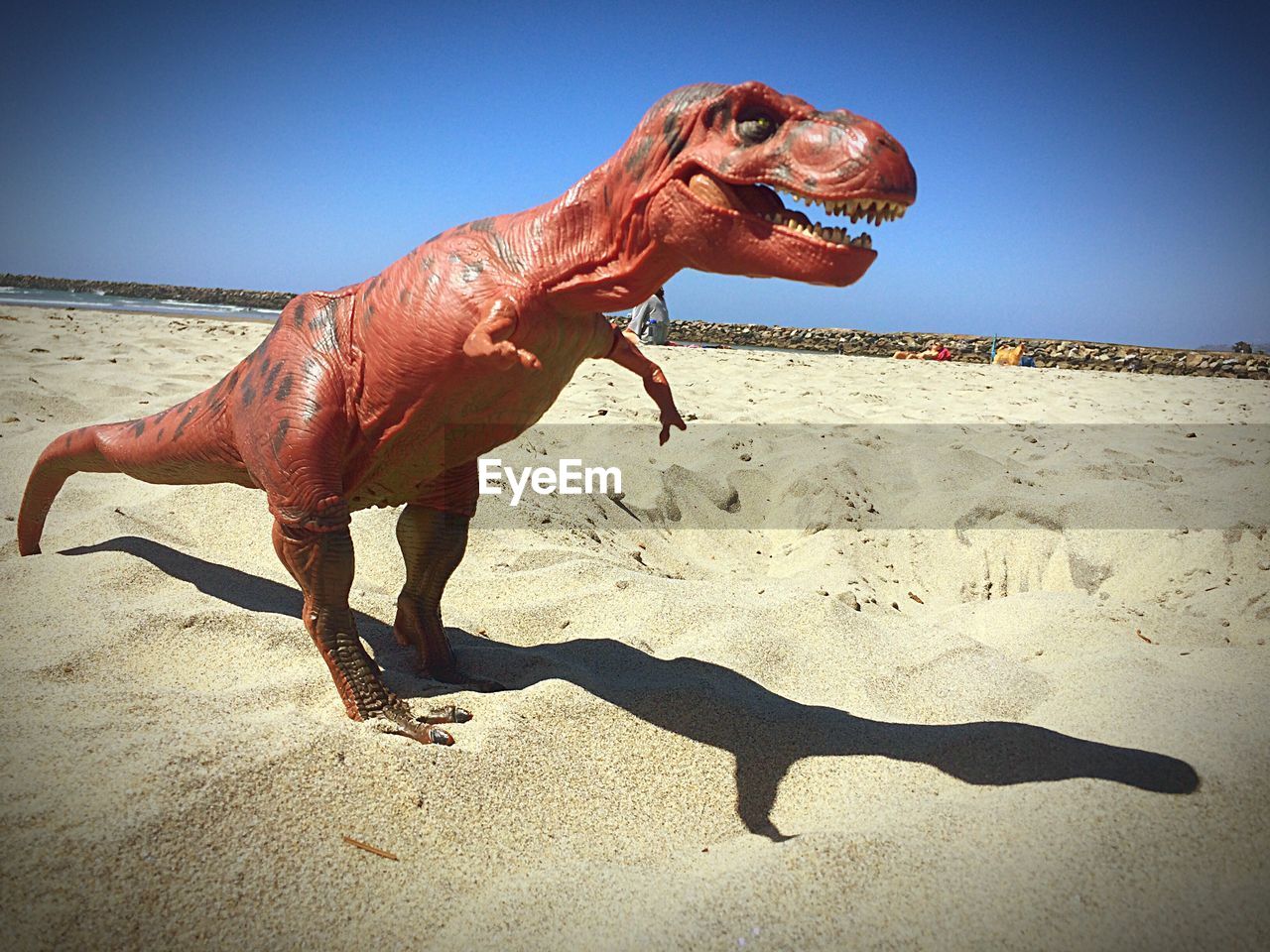 Dinosaur sculpture at beach against sky