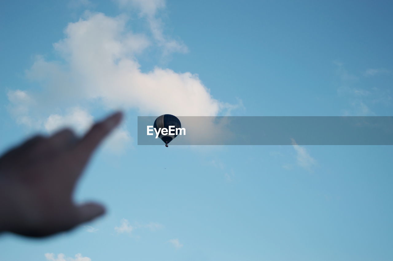 Cropped image of hand pointing at hot air balloon