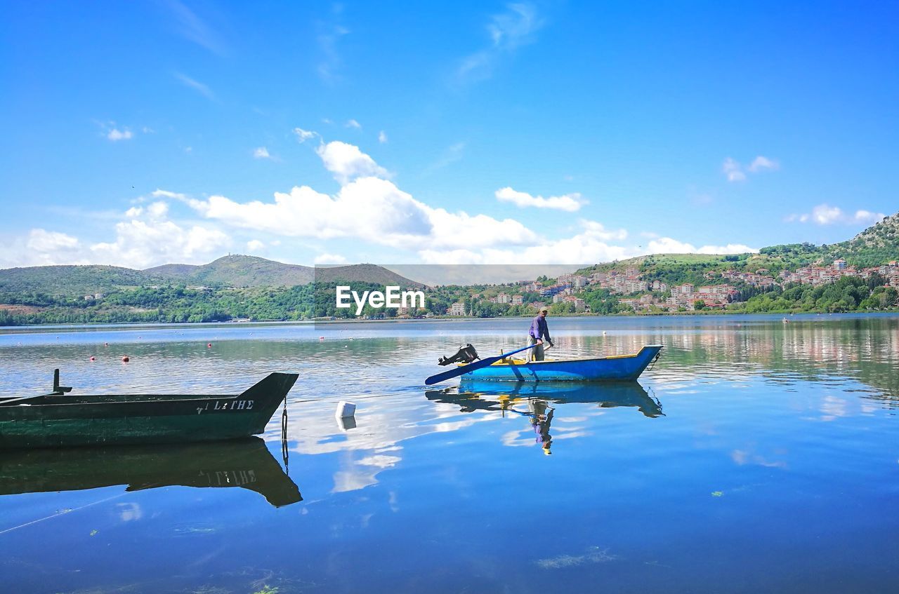 BOATS MOORED ON LAKE AGAINST BLUE SKY