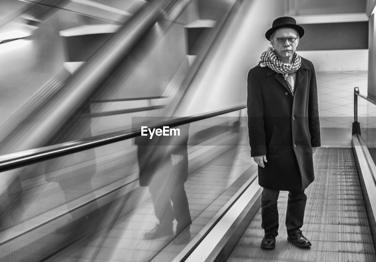 Full length portrait of senior man standing on moving walkway