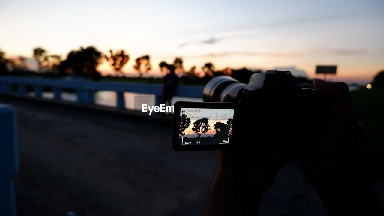 Man photographing with camera phone against sky during sunset