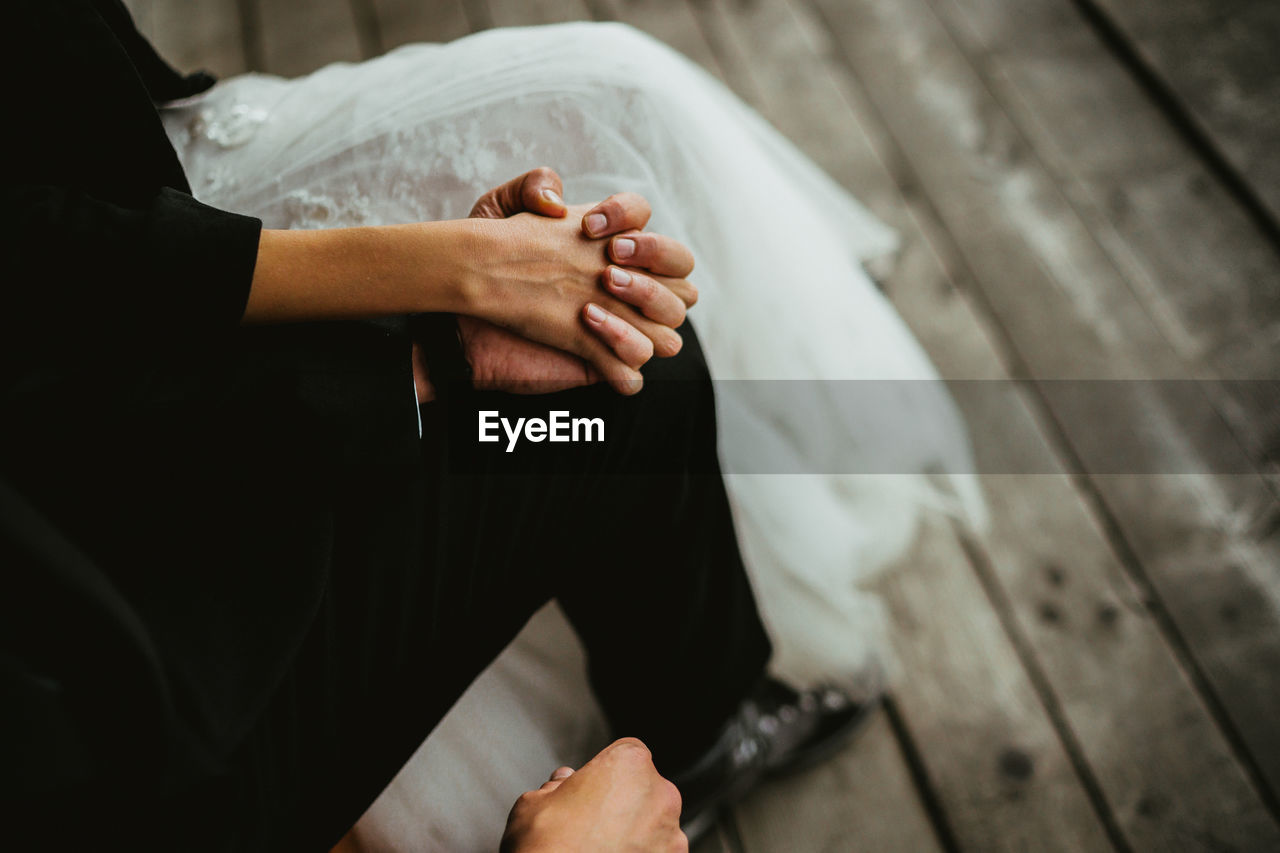 Low section of bride and bridegroom holding hands