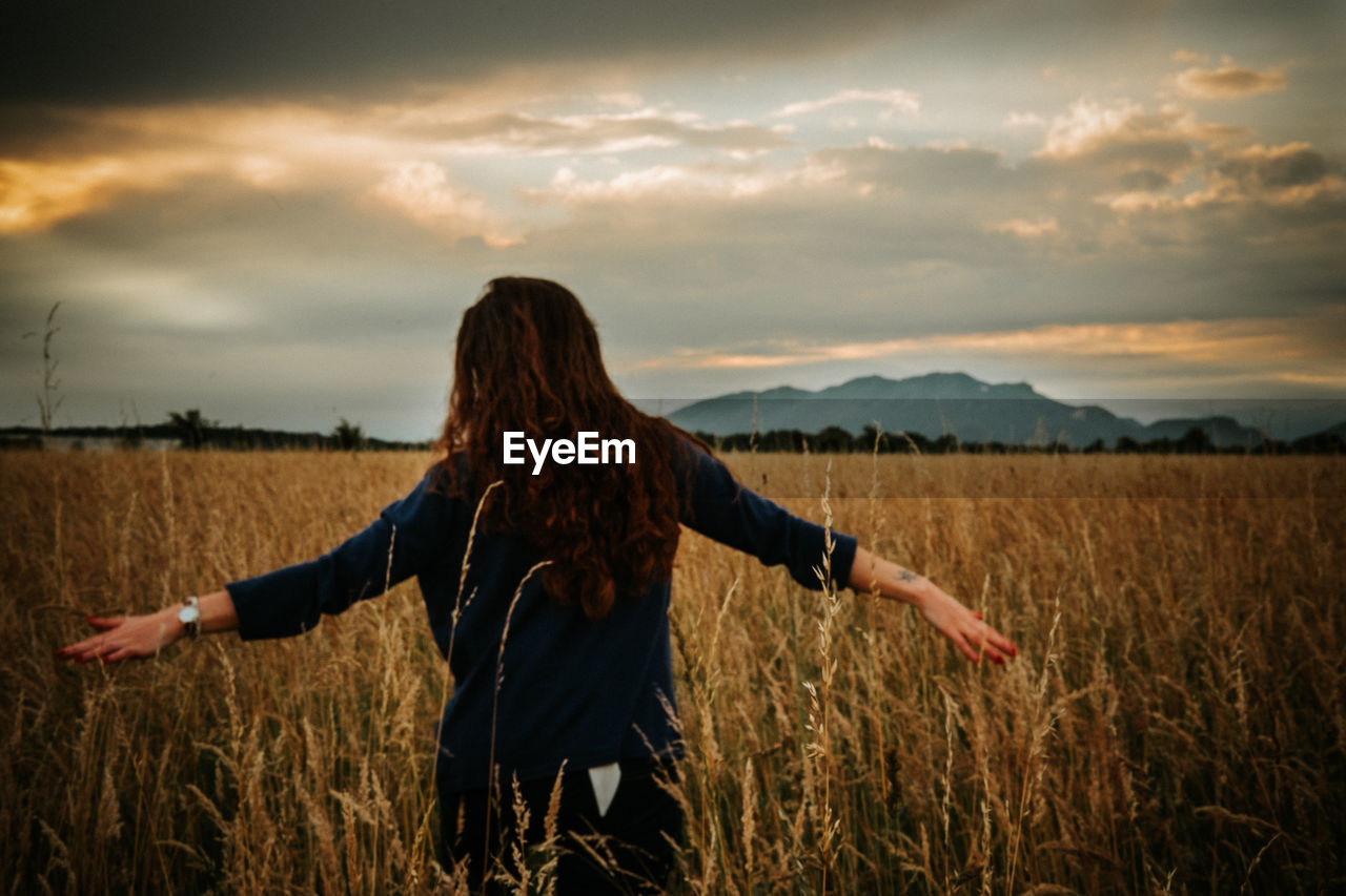 Woman with arms outstretched standing on field against sky