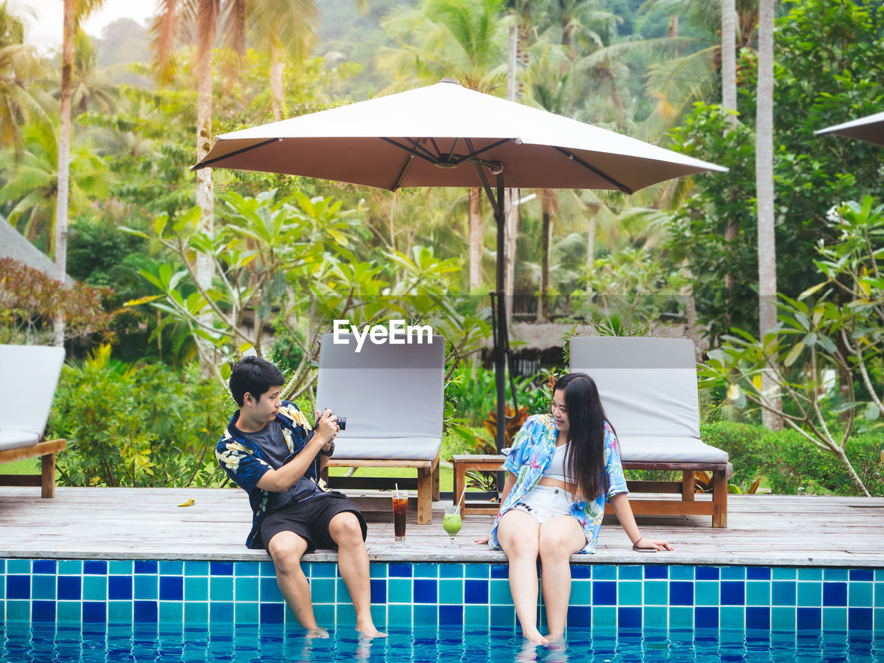 Young asian couple enjoying summer vacation travel photography beside swimming pool in the resort.