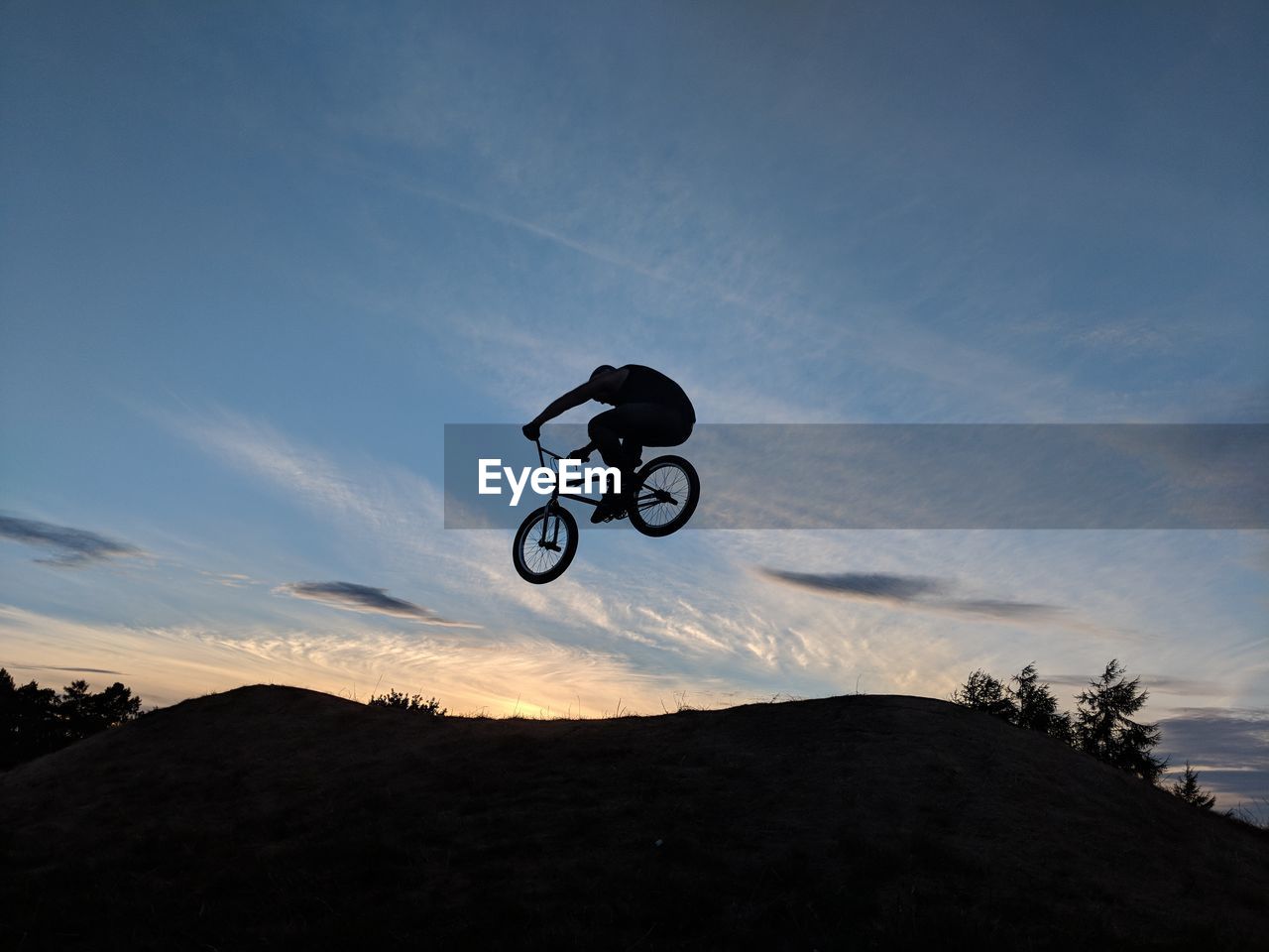 Low angle view of silhouette man performing stunt on bicycle against sky