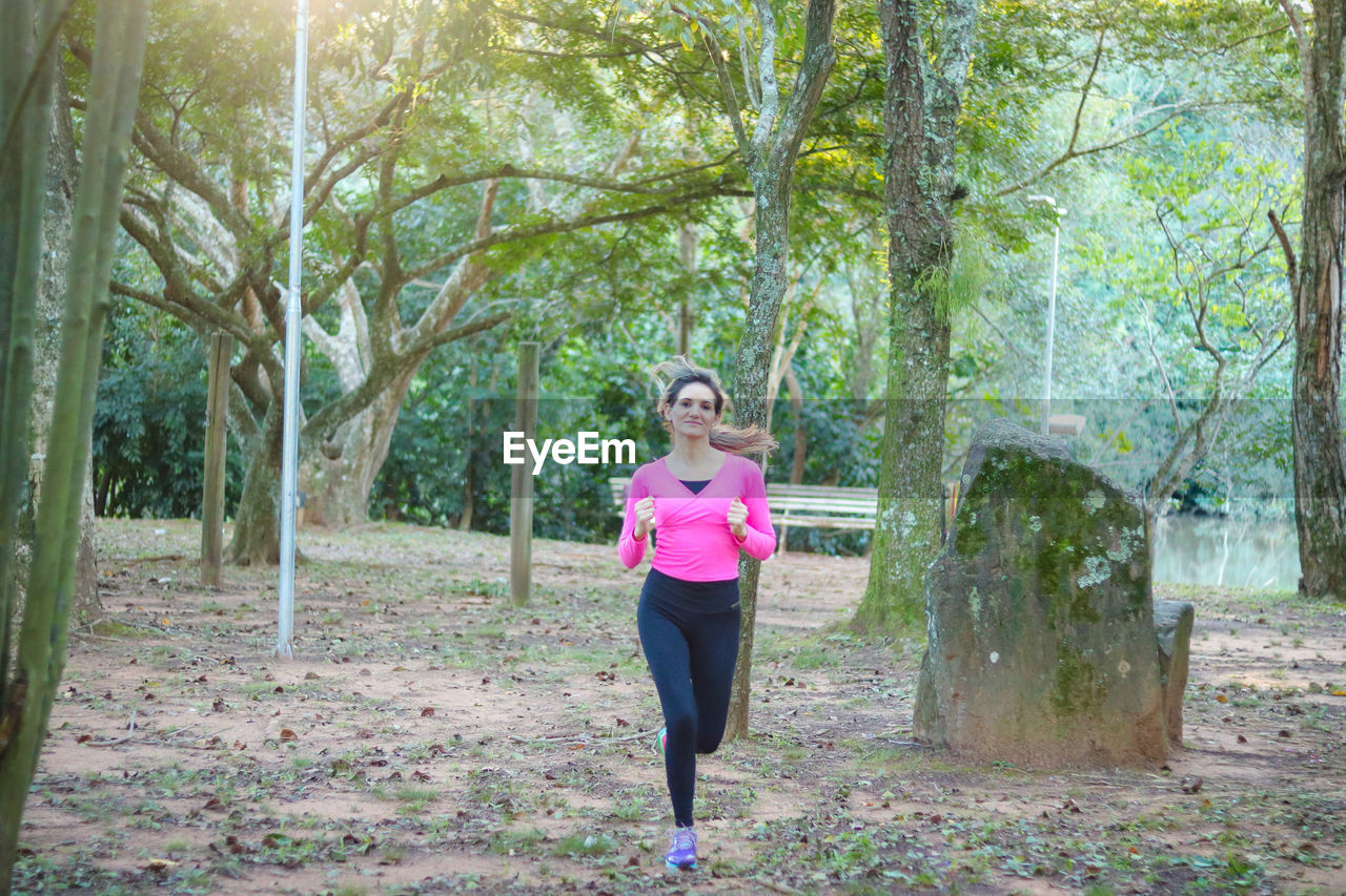 Young woman running against trees at park