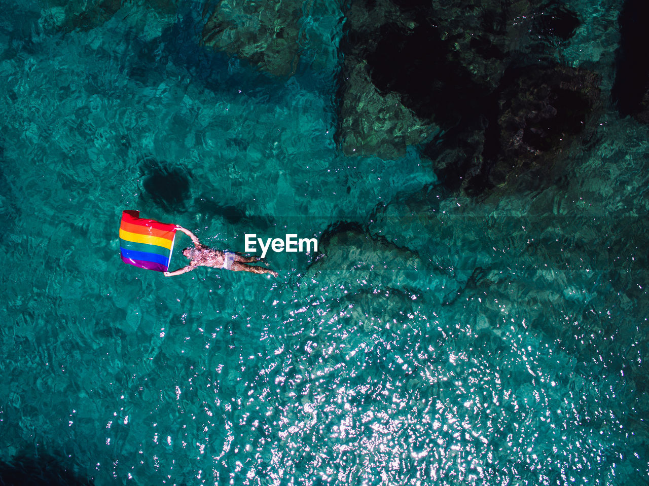 Aerial view of man swimming with rainbow flag