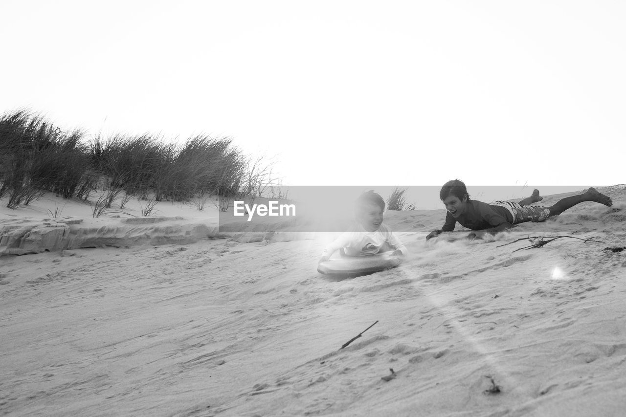 Brothers playing on sand at beach against clear sky