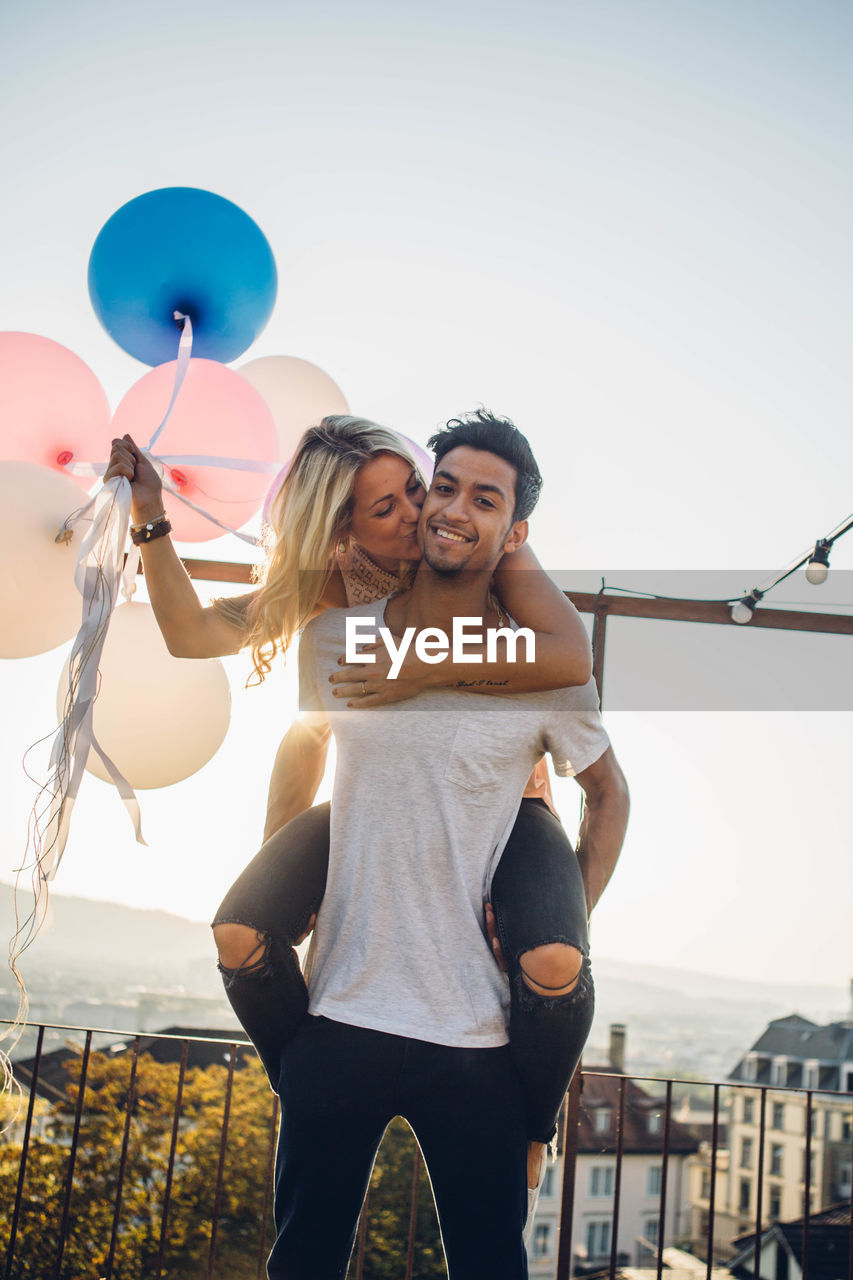 Couple standing with balloons against sky