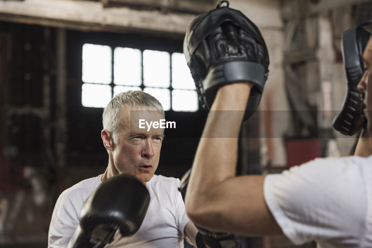 Determined senior male boxer practicing with friend in gym