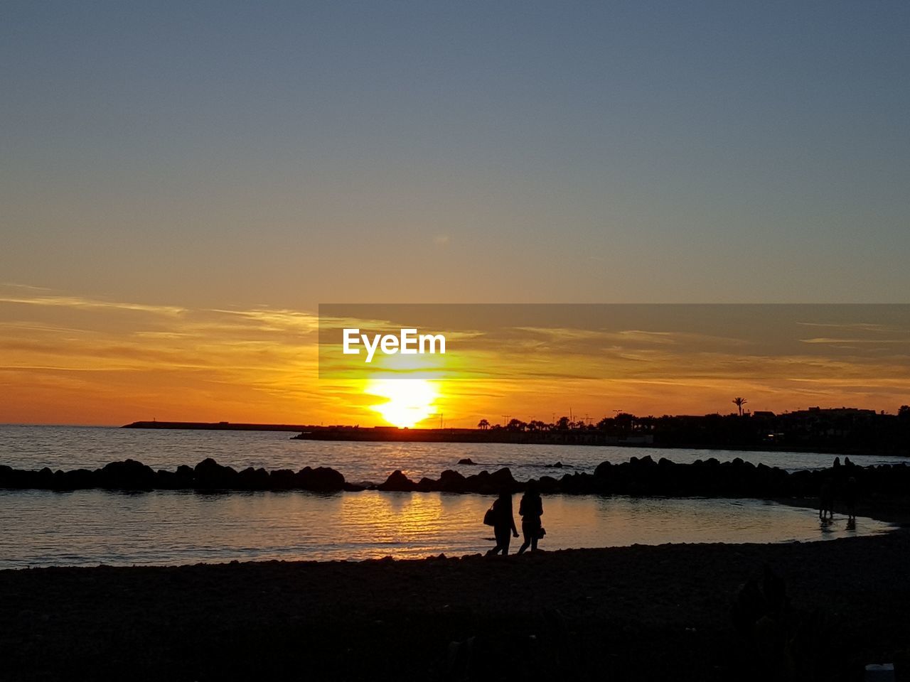 SILHOUETTE PEOPLE ON BEACH AGAINST ORANGE SKY