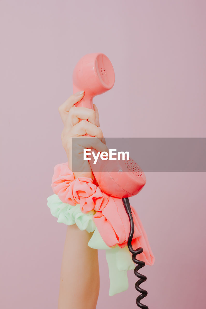 Close-up of hand holding telephone receiver against pink background