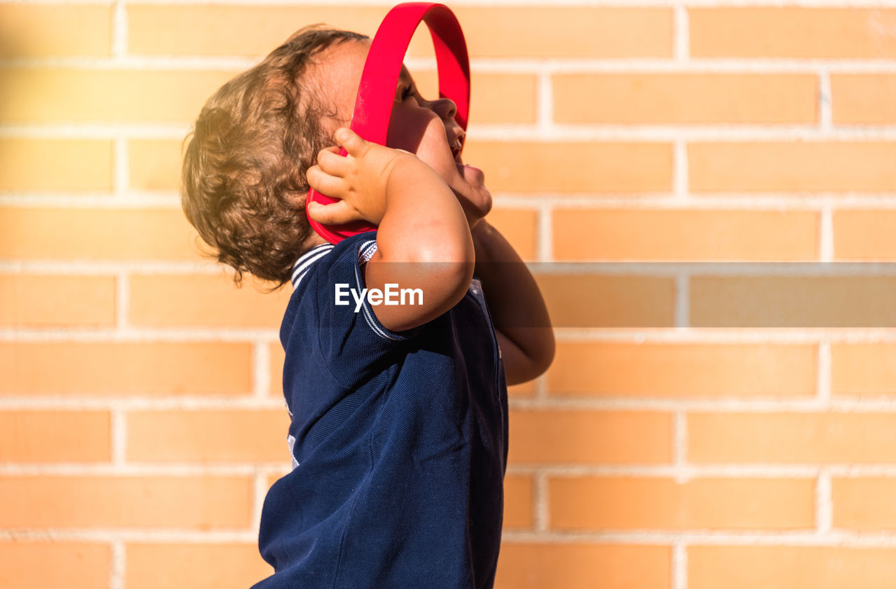 Portrait child listening to music with headphones on brick wall